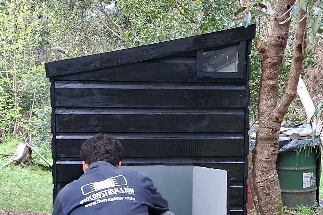 Caseta terminada, pintada de negro, con la puerta de acceso a la cámara abierta y el interior revestido en blanco.